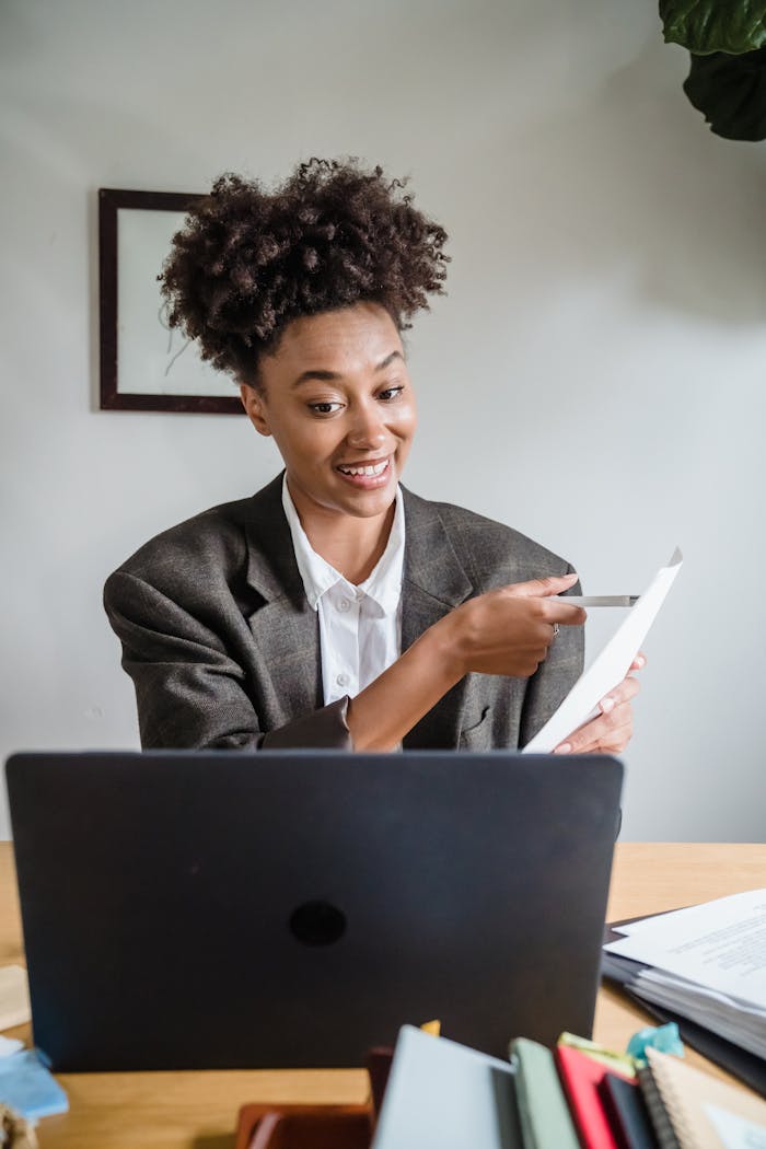 Businesswoman smiling and pointing at document during a video call in a modern office setting.